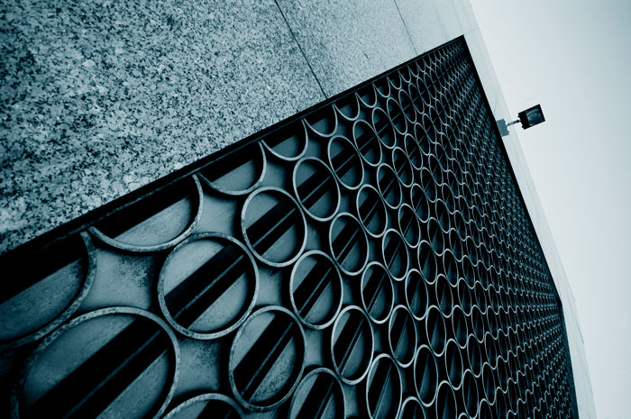 A picture of a grid, taken at an angle; its vanishing point leads up to a security camera.