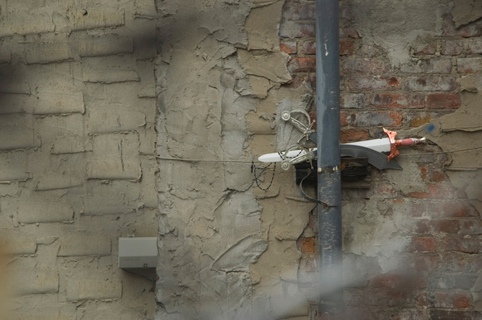 Three plastic children's swords have been stashed between a wall and a gutter pipe.