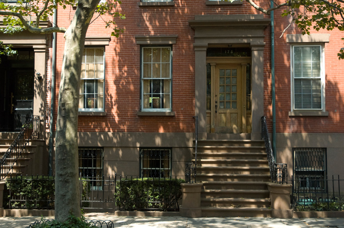 Trees speckle a brick house with their shadows.