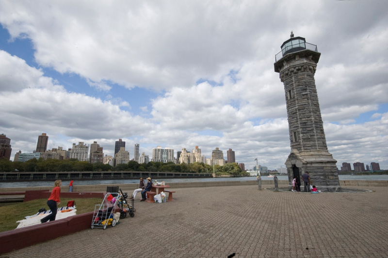 People are gathered in a park surrounding an old lighthouse.