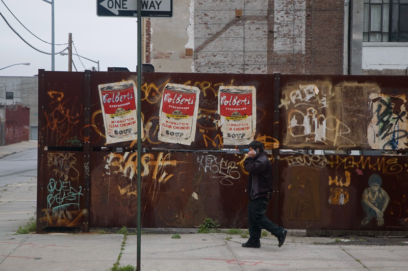 A man walks past Warhol-like soup posters of soup with Stephen Colbert's name on them.