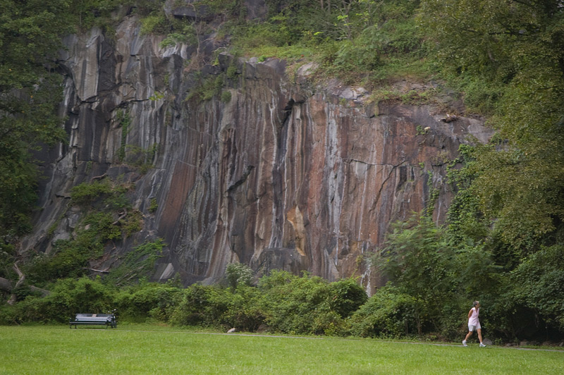 A cliff in a park, with a walker on the path.