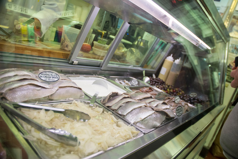 Smoked herring behind a deli counter's glass, with cream and onions.